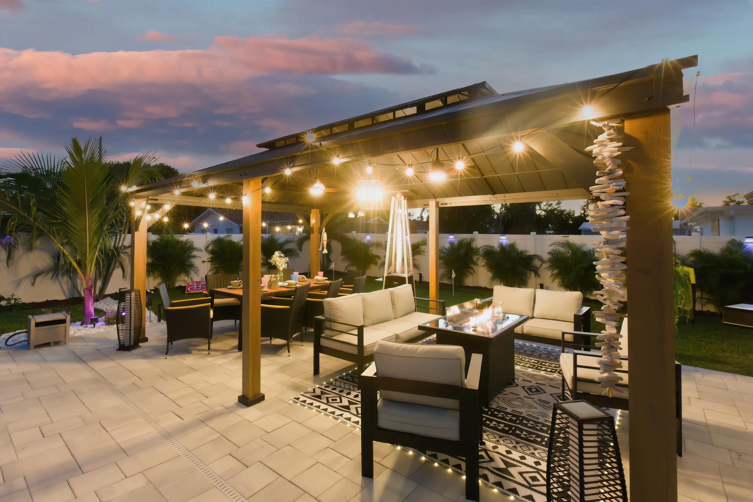 Een terras buiten met een pergola, een zitgedeelte en lichtslingers.