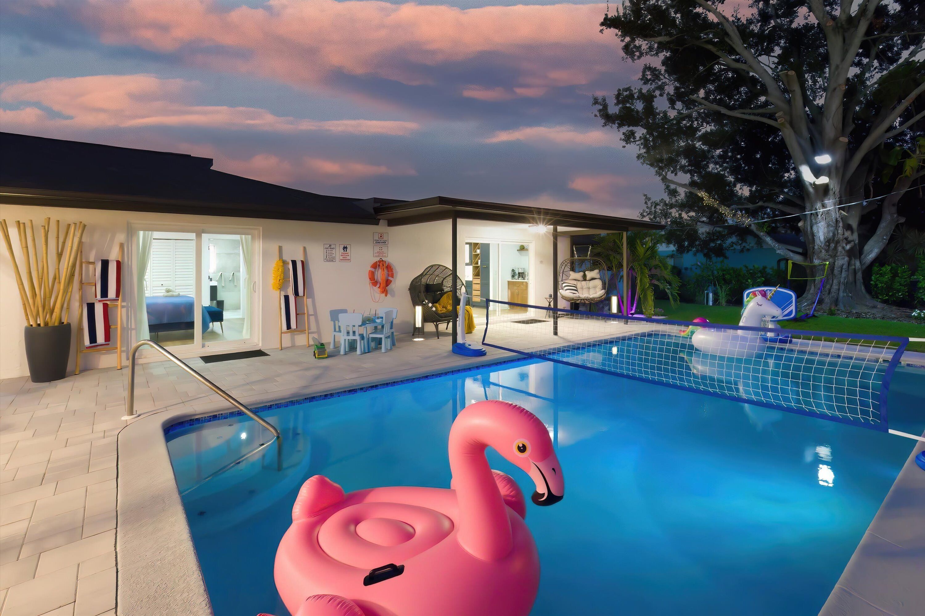 Een binnenzwembad met een roze flamingo drijver, een boom en een huis met een glazen deur.