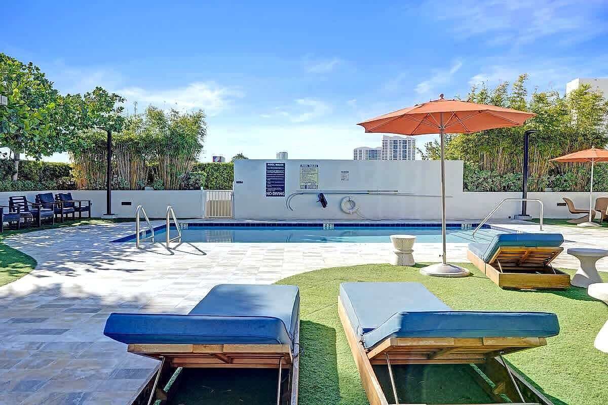 Un área de piscina en la azotea con sillones de descanso, sombrillas y un bar junto a la piscina.