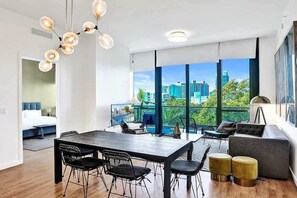 A modern hotel room with a dining area, large windows with a city view, and a balcony with outdoor seating.