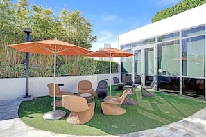 An outdoor seating area with wicker furniture and orange umbrellas, surrounded by a manicured lawn and bamboo plants. - 17West 3BR Miami Beach | Pool & Walk to Beach (Miami Beach)