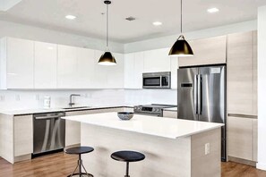 A modern kitchen with white cabinetry, stainless steel appliances, and a central island with stools.
