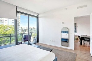 Una camera da letto moderna con un letto grande, una porta scorrevole in vetro che dà su un balcone, un'area pranzo con tavolo e sedie e uno specchio a parete.