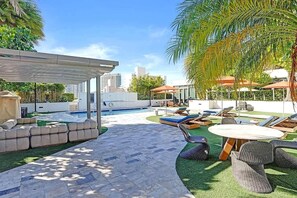 Area piscina sul tetto con sedie a sdraio, una zona relax coperta e vista sullo skyline della città.