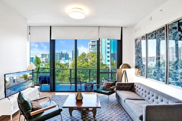 A modern living room with a large window, a sofa, a coffee table, and a television.