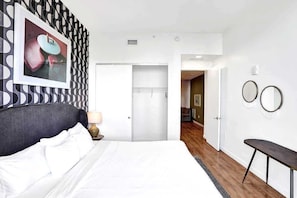 A hotel room with a bed, a bedside table, a lamp, a wardrobe, and a mirror on the wall. - 17West 3BR Miami Beach | Pool & Walk to Beach (Miami Beach)