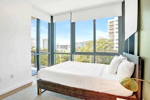 A bedroom with a large window, a bed, and a lamp.