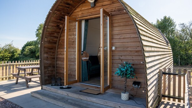 A wooden cabin with a curved roof, a welcome sign, a bench, and a potted plant outside.