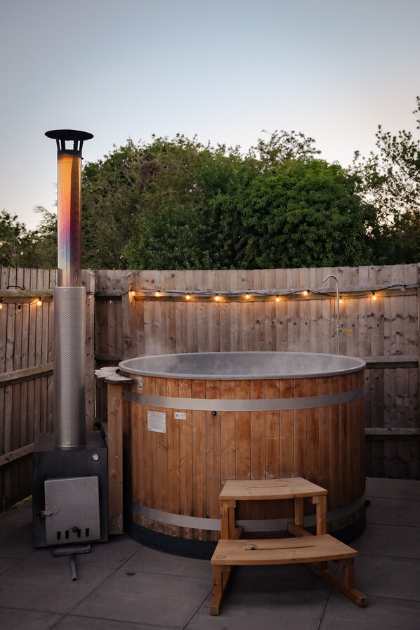 A hot tub with a wooden exterior, a metal heater, and a small wooden stool.