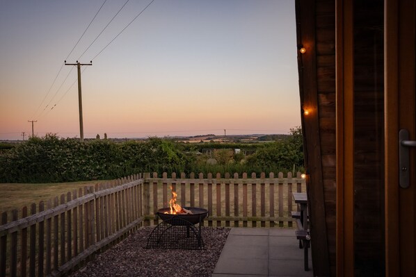 A patio with a fire pit, a wooden fence, and a view of the countryside.