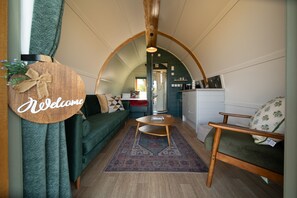 Un intérieur chaleureux avec un plafond voûté, un panneau d’accueil, un canapé, une petite table et un coin cuisine.