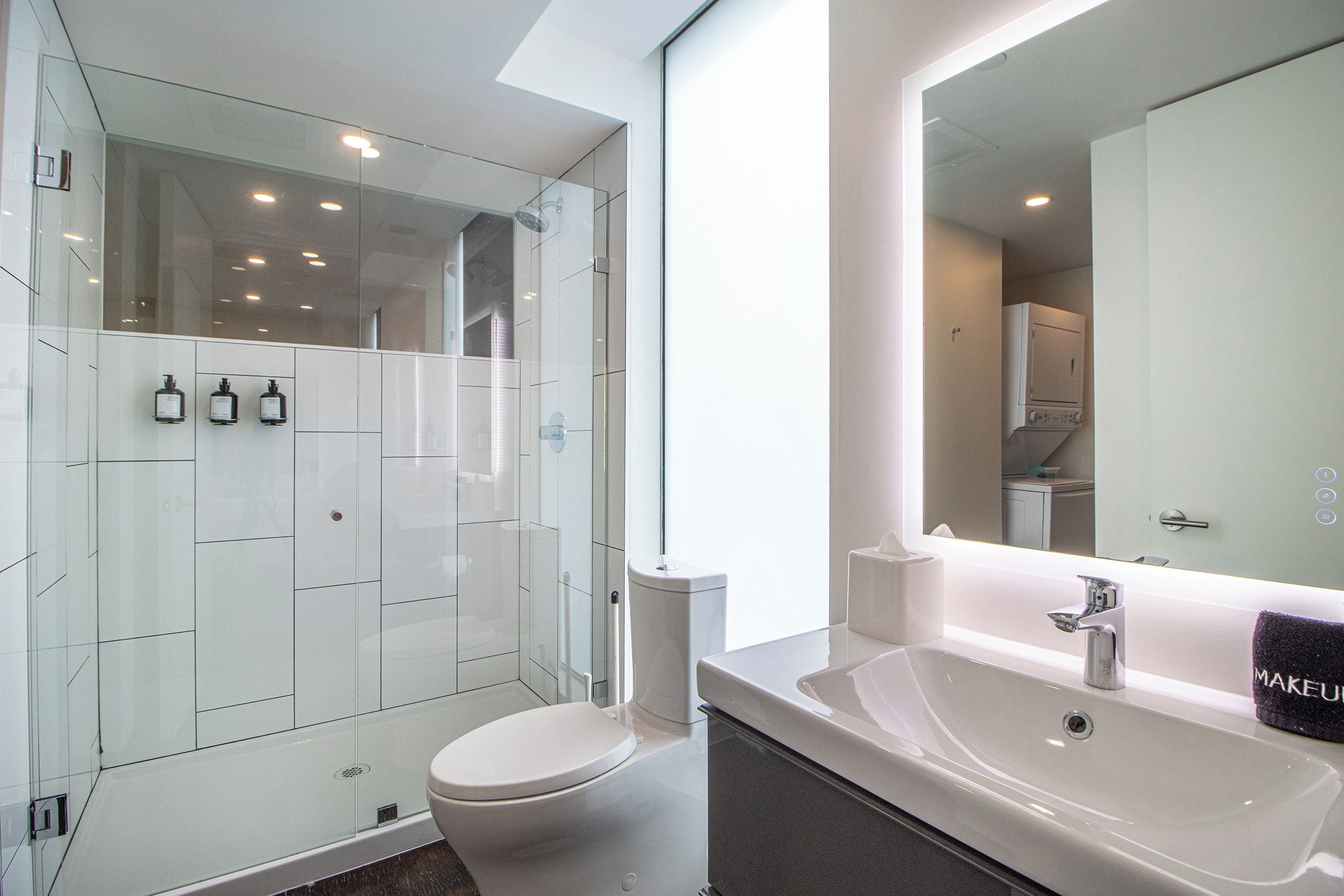 A modern bathroom with a glass shower enclosure, a white toilet, a sink with a mirror, and toiletries on the wall.