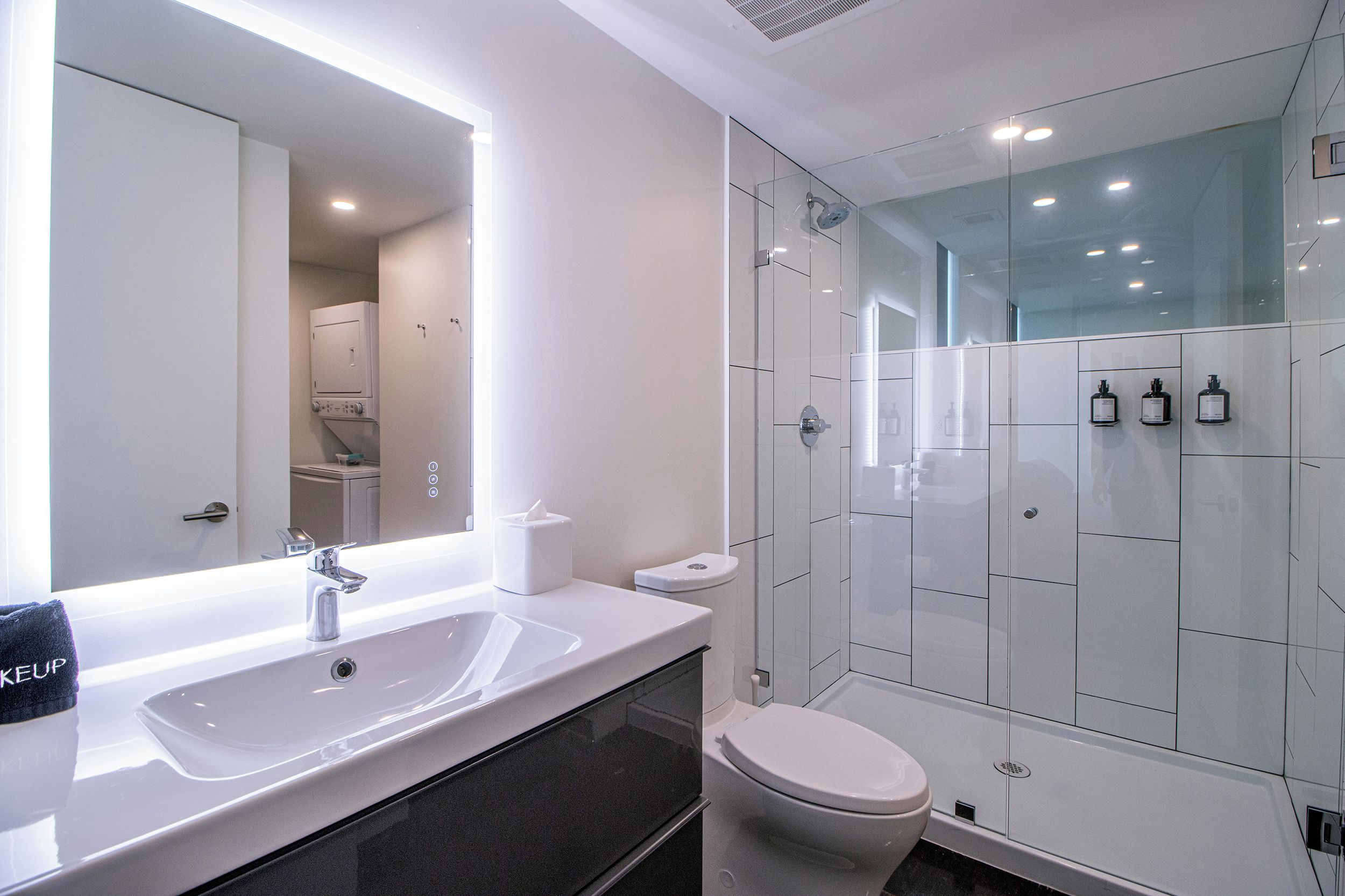 A modern bathroom with a large mirror, a sink, a toilet, and a glass-enclosed shower.