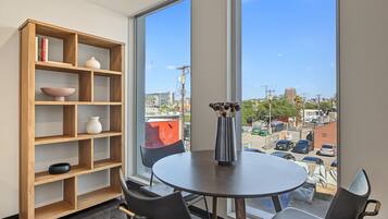 A room with a large window, a round table, two chairs, a bookshelf, and a vase with flowers.