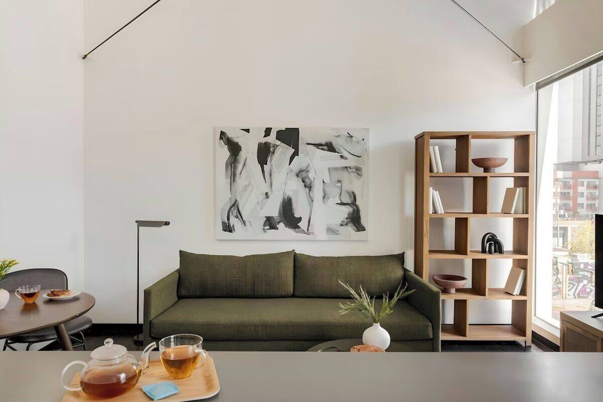 Un moderno salón con un sofá verde, una mesa de centro con una tetera y una taza, una estantería y un cuadro abstracto grande en la pared.