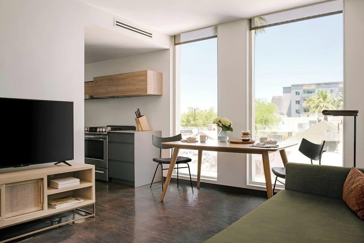 Una sala moderna con televisor de pantalla plana, mueble de entretenimiento de madera, mesa de comedor con sillas y un sofá verde.