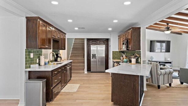 A modern kitchen with wooden cabinets, a stainless steel refrigerator, and a central island. - Luxury Estate with Pool & Game Room (Kemah Area)