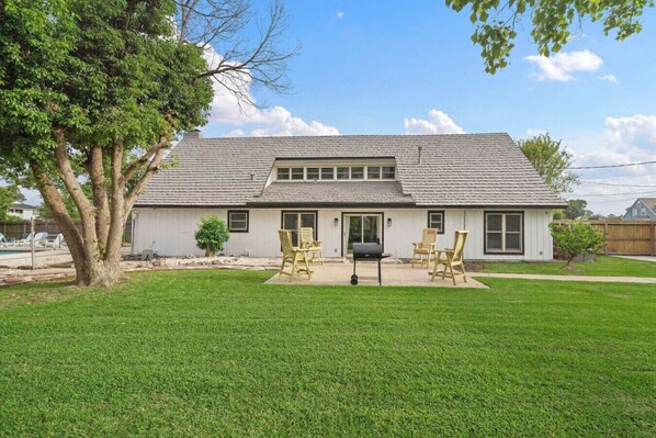 A two-story house with a covered patio, a swimming pool in the background, and a well-maintained lawn.