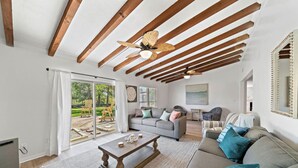 A spacious living room with a large sofa, a coffee table, and a ceiling fan. There is a sliding glass door leading to an outdoor area with chairs. - Luxury Estate with Pool & Game Room (Kemah Area)