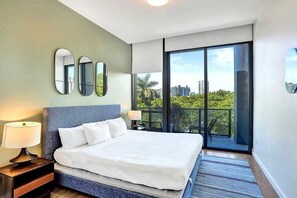 Une chambre d’hôtel avec un grand lit, une table de chevet, une lampe, un balcon avec vue sur la ville et trois miroirs muraux.