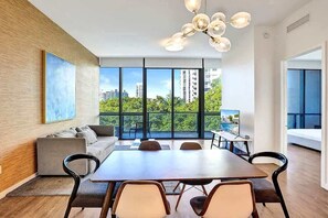 A modern living room with a large dining table, comfortable seating, a sofa, and a view of the city through large windows.