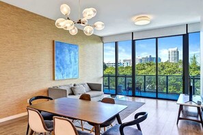 A modern room with a dining table, chairs, a sofa, and a large window offering a city view.