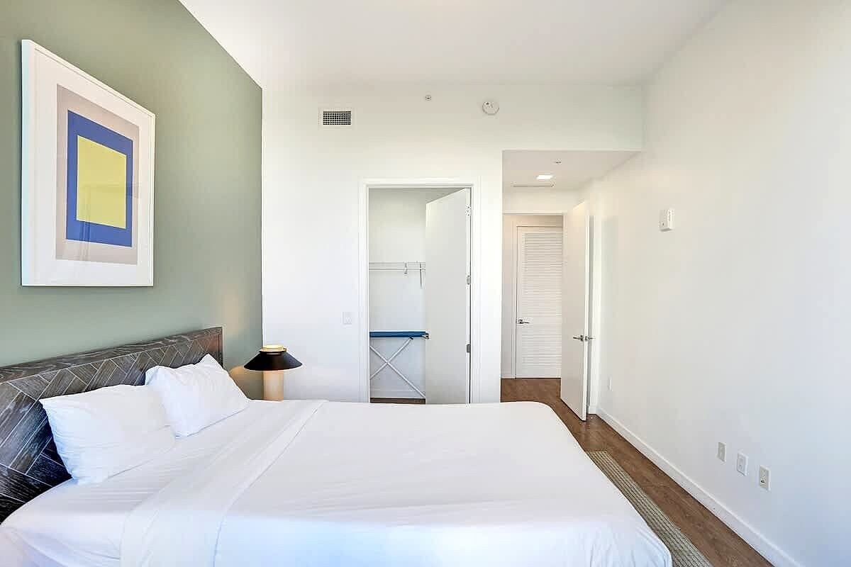 A hotel room with a large bed, a bedside table, a framed picture on the wall, and a door leading to a bathroom.