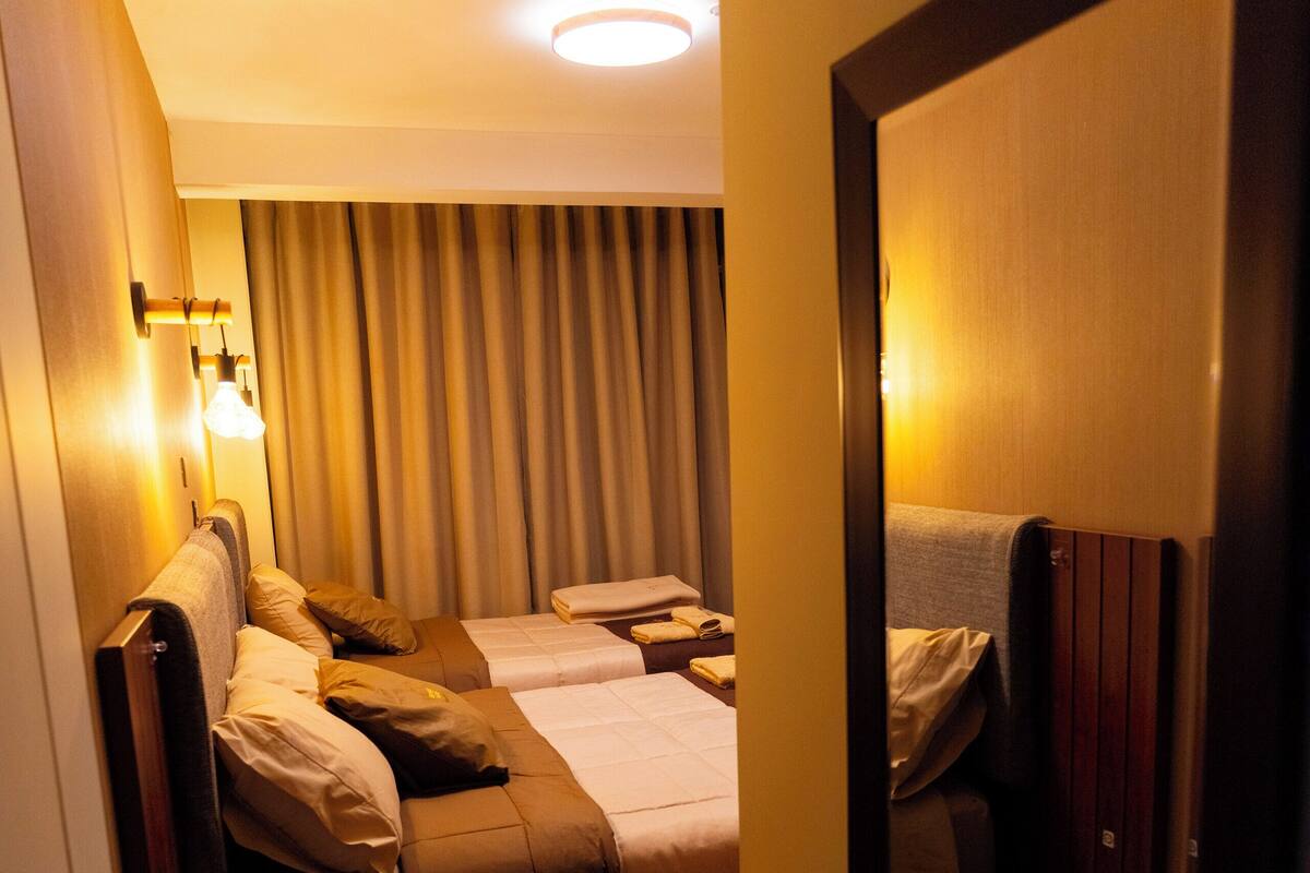 Hotellihuone, jossa on kaksi sänkyä, suuri peili ja puulattia.