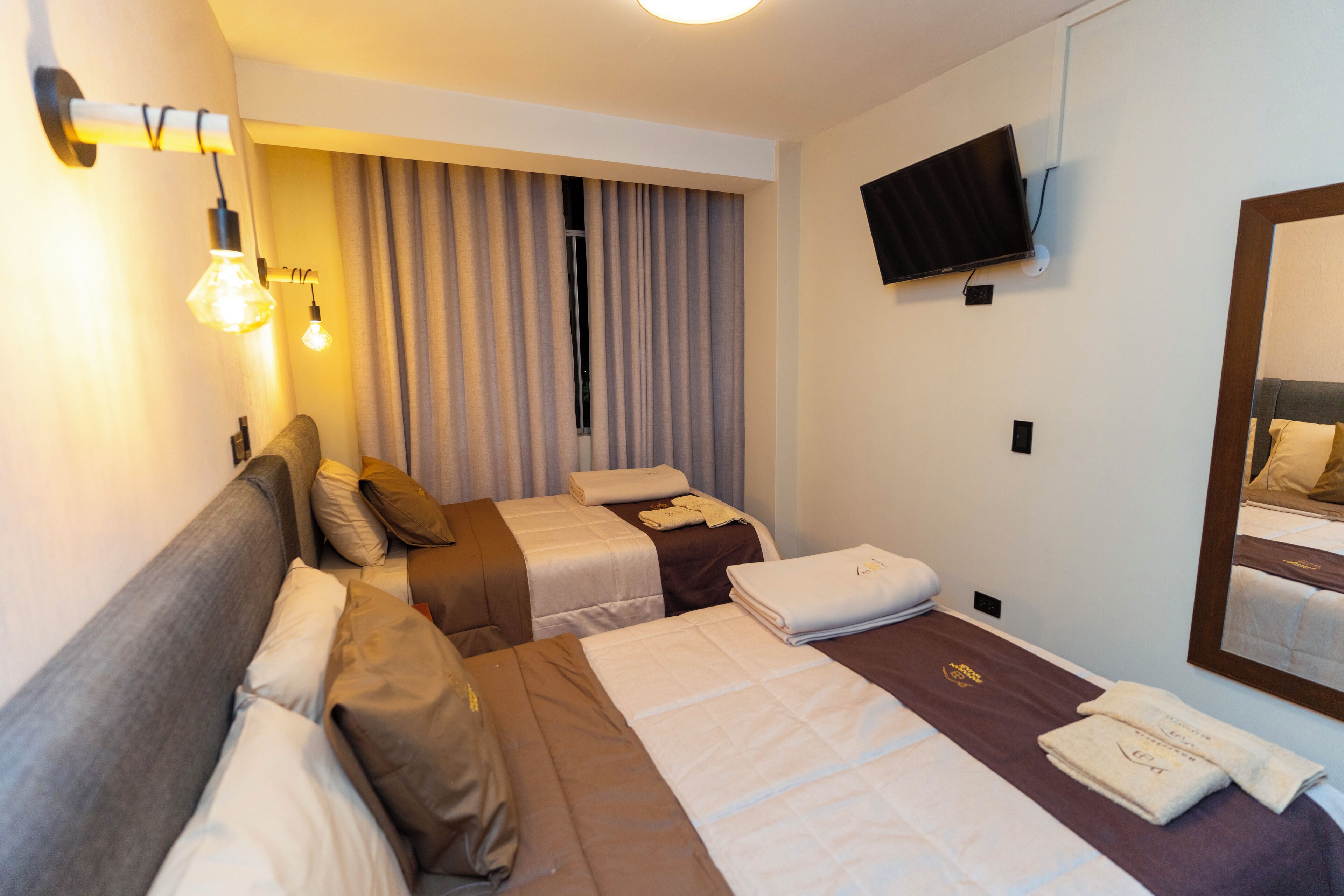 A hotel room with two single beds, a flat-screen TV, and a large mirror.