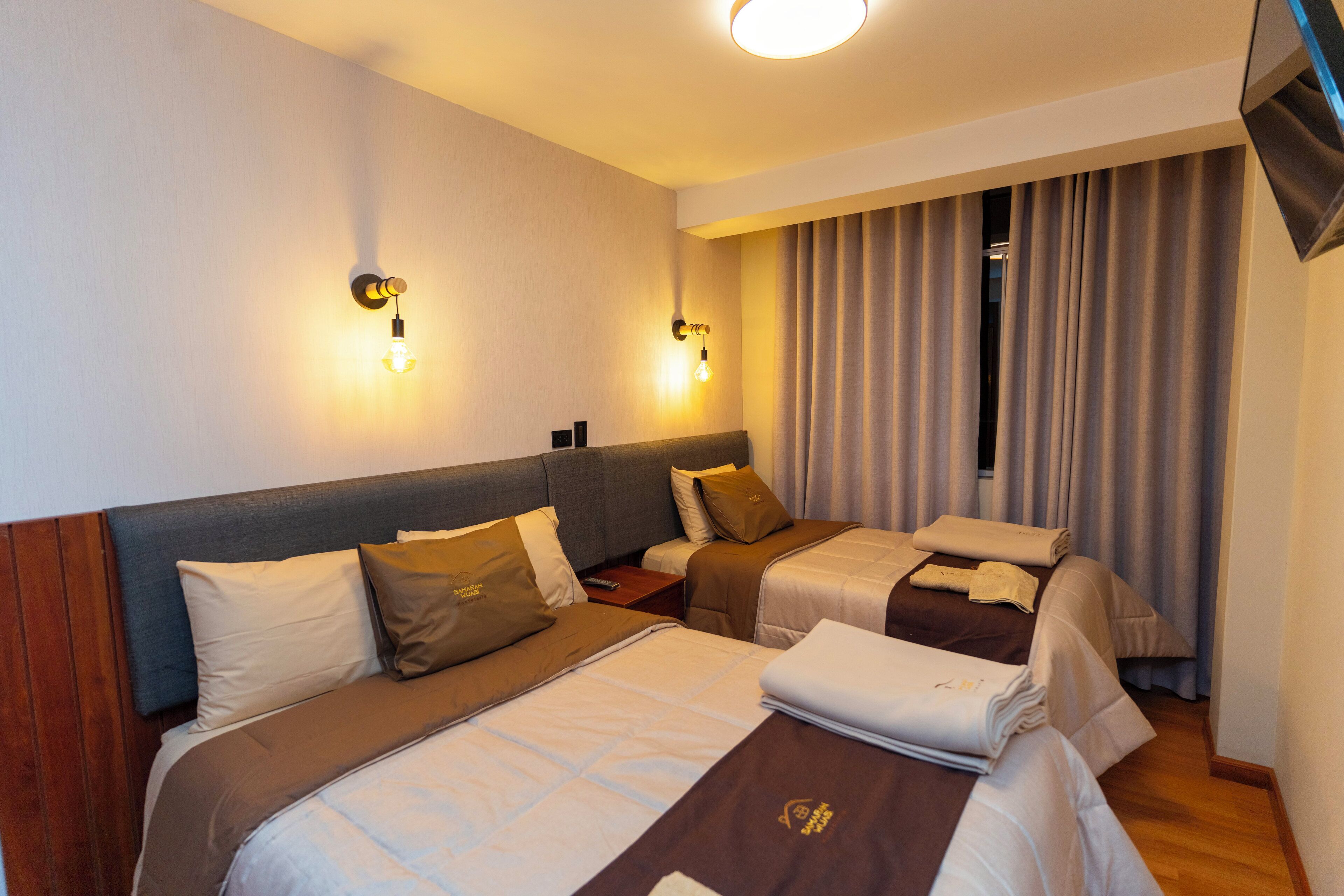 Een hotelkamer met twee bedden, een televisie en een raam met gordijnen.