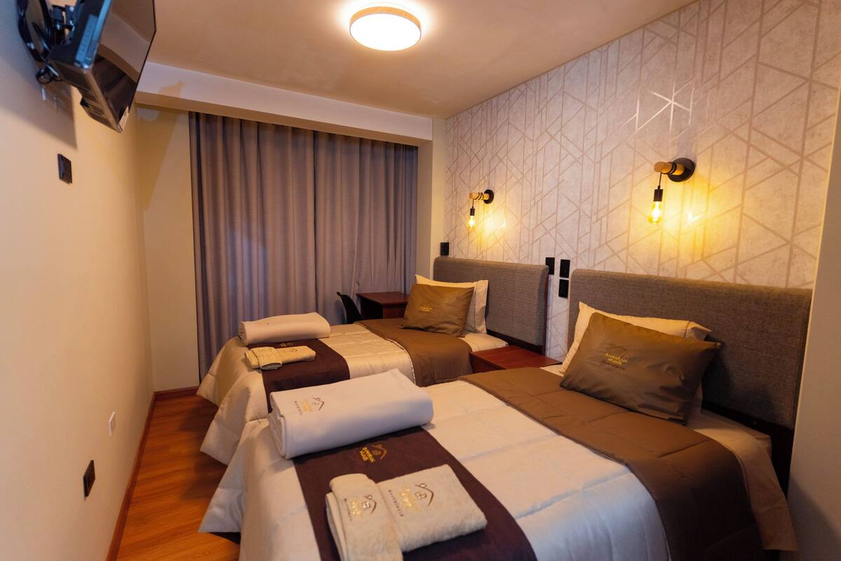 Hotellihuone, jossa on kaksi sänkyä, seinälle asennettu televisio ja verho.