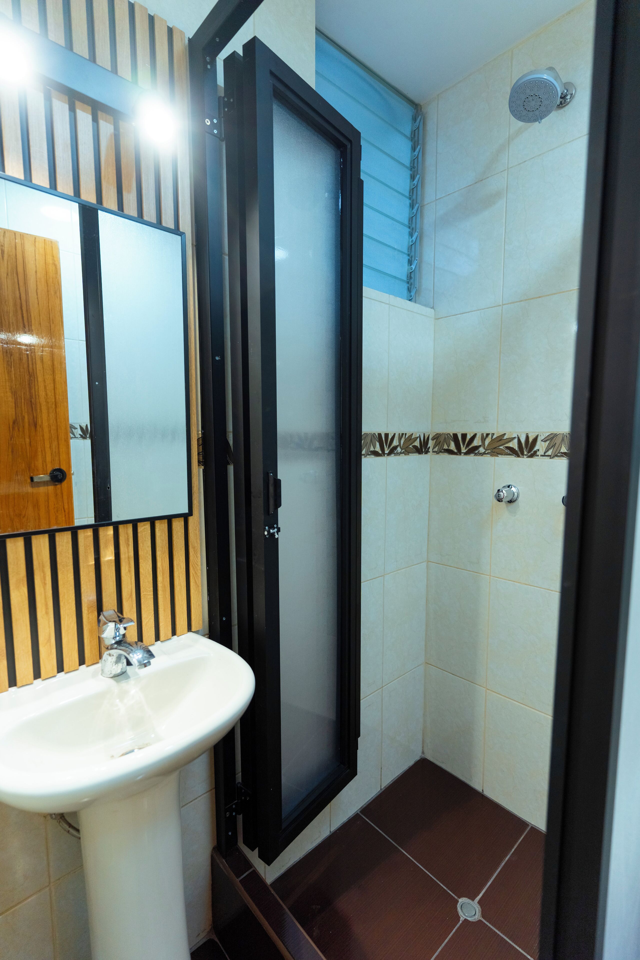 A bathroom with a sink, mirror, shower, and tiled walls.