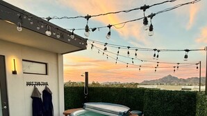 Uma banheira de hidromassagem em um deck de madeira, com luzes de festa, uma cadeira e uma mesa.