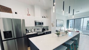 Cozinha moderna com eletrodomésticos de aço inoxidável, uma ilha central com banquetas e uma grande janela com vista para a cidade.