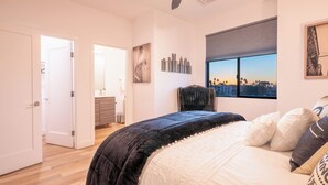Quarto com uma cama grande, vista para a cidade, ventoinha no teto e porta para outro cômodo.