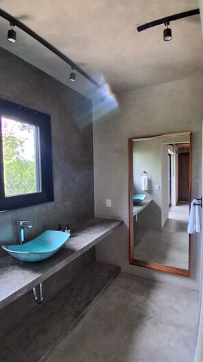 Une salle de bain moderne avec un grand miroir, un lavabo aux lignes courbes et une fenêtre laissant entrer la lumière naturelle.