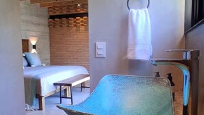 A bathroom with a large, textured basin, a bed with a wooden headboard, and a brick wall. - The sea in front of your window! (Puerto Vallarta)