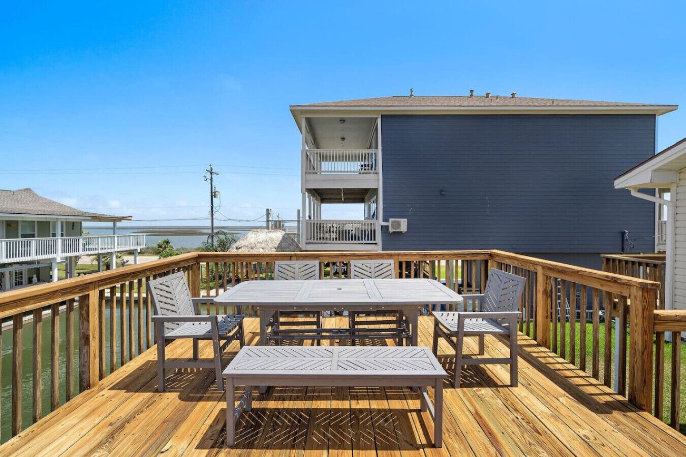 Een houten terras met een tafel en stoelen, met uitzicht op een waterpartij en een gebouw met een balkon.