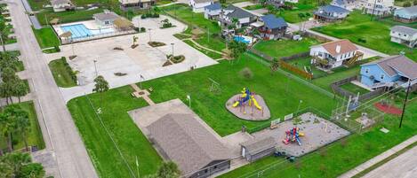 An aerial view of a residential area with houses, a playground, and a swimming pool.
