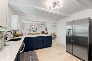Et moderne køkken med en central ø, rustfrie hvidevarer og en lysekrone.