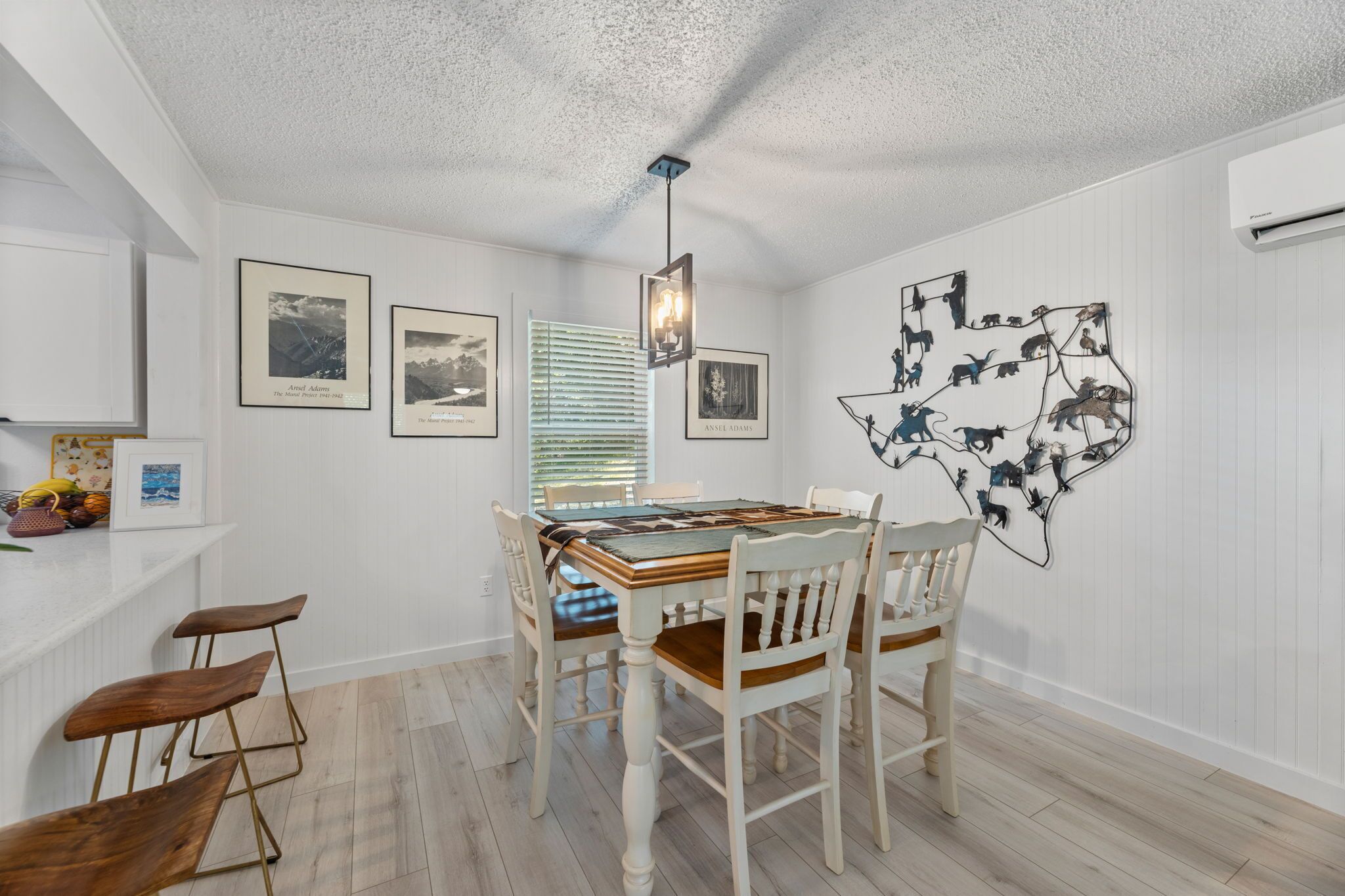 A dining area with a wooden table, white chairs, and framed pictures on the wall.