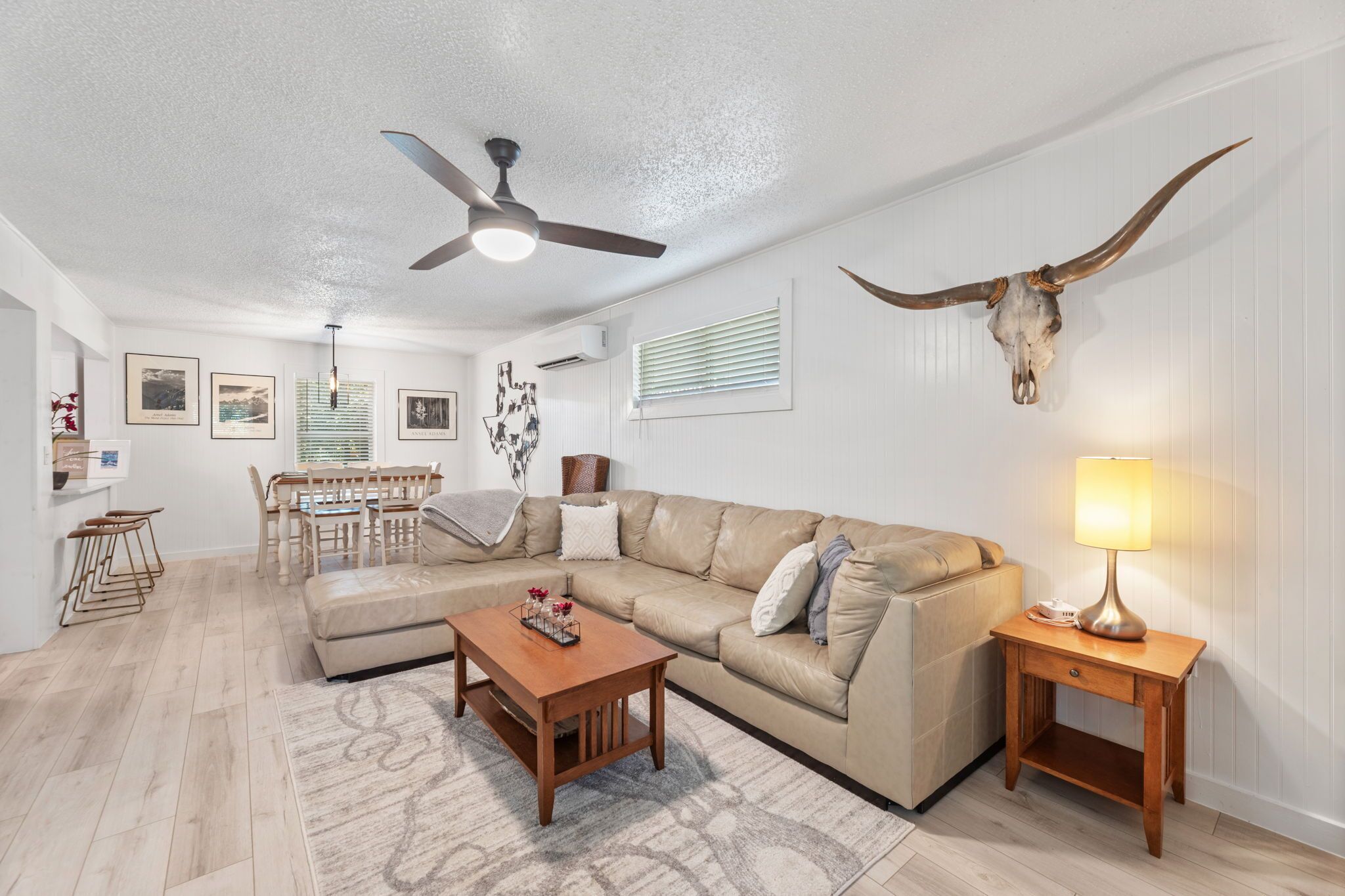 A living room with a beige sofa, a wooden coffee table, a ceiling fan, and a wall-mounted bull skull.