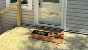 Una casa con un porche de madera, una puerta corrediza de vidrio y un felpudo que dice 'Hola' y 'so'.
