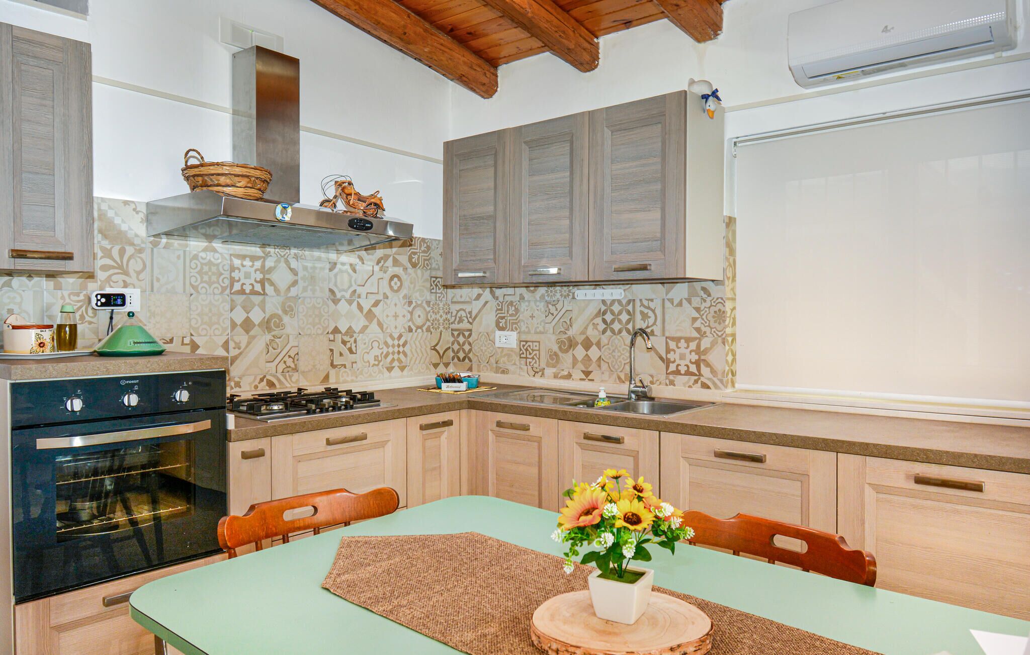 A kitchen with a stove, oven, and sink, wooden cabinets, patterned backsplash, and a dining table with chairs.