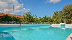 En klar swimmingpool med flisekant, omgivet af en stenvæg og træer.