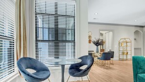 A modern living room with a round glass table, two blue chairs, a teal sofa, and a dining area with a gold-framed table and chairs. - Cozy 2-bedroom condo in serene Atlanta with AC and fitness room (Atlanta)