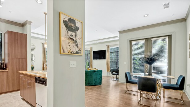 A modern kitchen with a dishwasher, a dining area with a round table and chairs, and a large window with blinds. - Cozy 2-bedroom condo in serene Atlanta with AC and fitness room (Atlanta)
