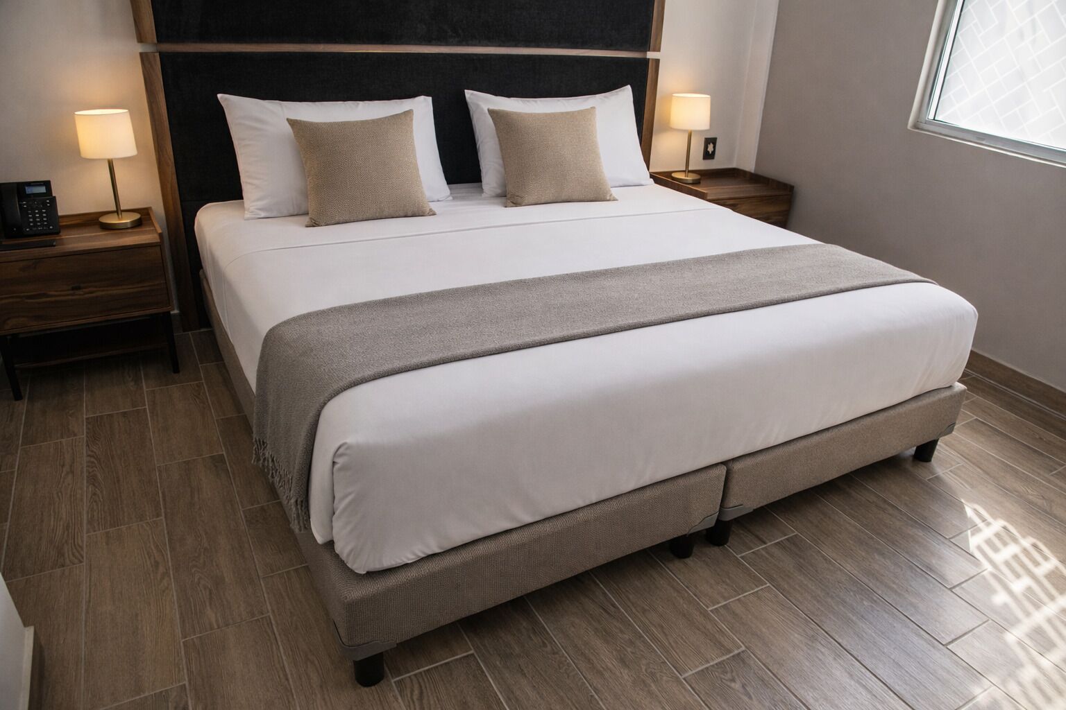 A large bed with a headboard, two bedside tables with lamps, and a window with blinds.
