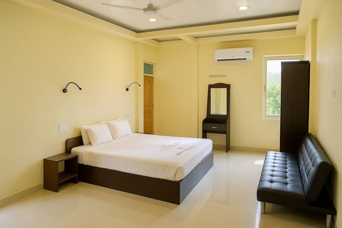 A hotel room with a bed, bedside table, dresser, mirror, and a bench.