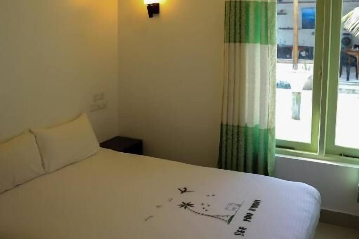 A hotel room with a bed, a nightstand, a wall-mounted lamp, and a window with curtains.